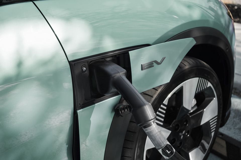 Close de um cabo de carregamento conectado à porta de carregamento frontal de um SUV elétrico Mitsubishi ASX 2027 verde menta, com um emblema EV na aba aberta