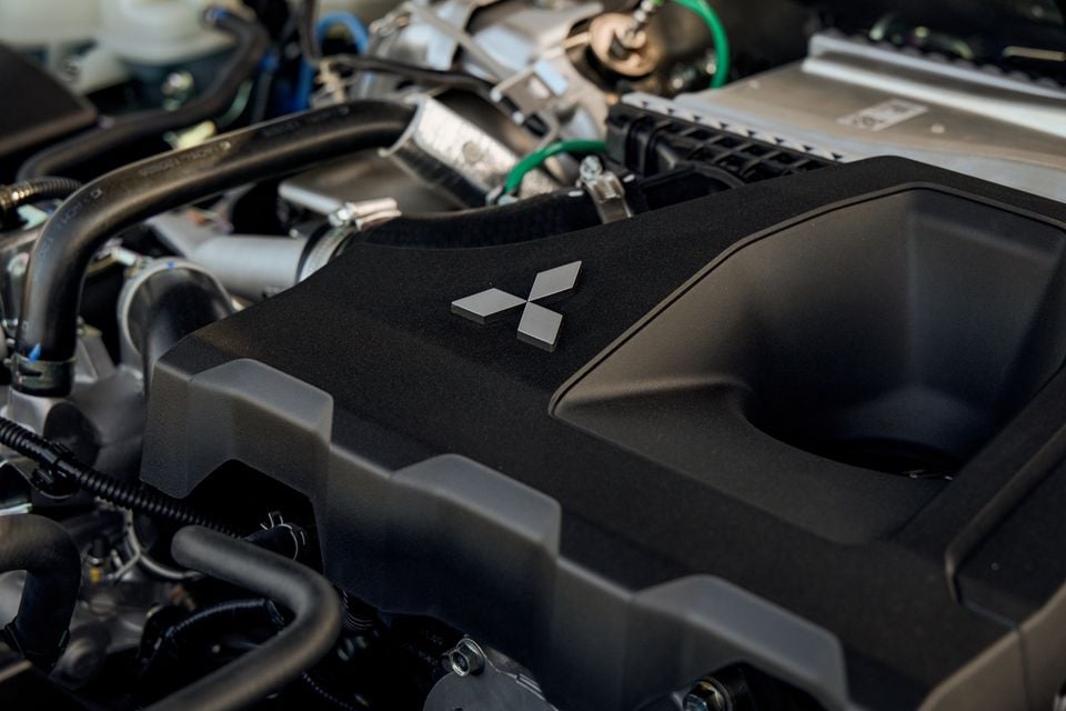 Engine cover with a Mitsubishi diamond logo in the engine bay of a 2027 Mitsubishi Pajero, surrounded by hoses and an intercooler