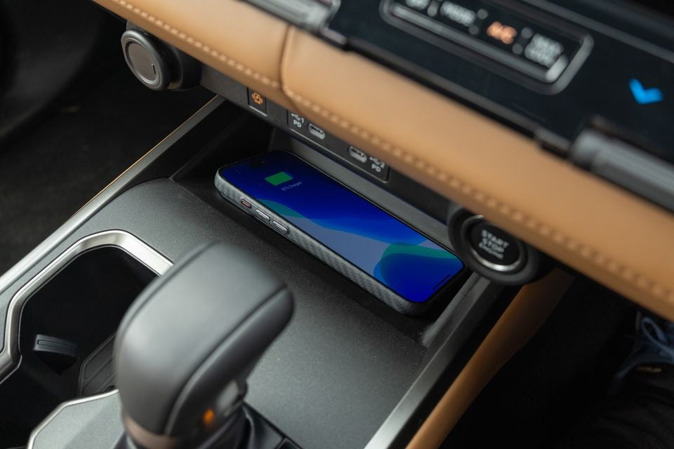 Smartphone charging on the wireless charging pad in the centre console of a 2027 Mitsubishi Pajero, beside the gear selector, USB-C ports and start button