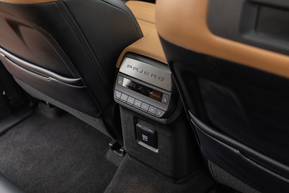 Rear climate controls and a 150W power outlet on the back of the centre console in a 2027 Mitsubishi Pajero, between tan and black leather front seats