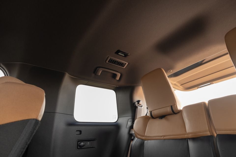 Rear cabin of the 2027 Mitsubishi Pajero showing tan and black leather seats, a roof-mounted air vent and a third-row side window