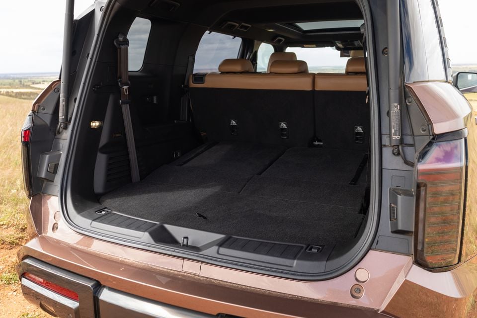 Boot of a bronze 2027 Mitsubishi Pajero with the third-row seats folded flat, showing the carpeted load floor and tan leather second-row seats