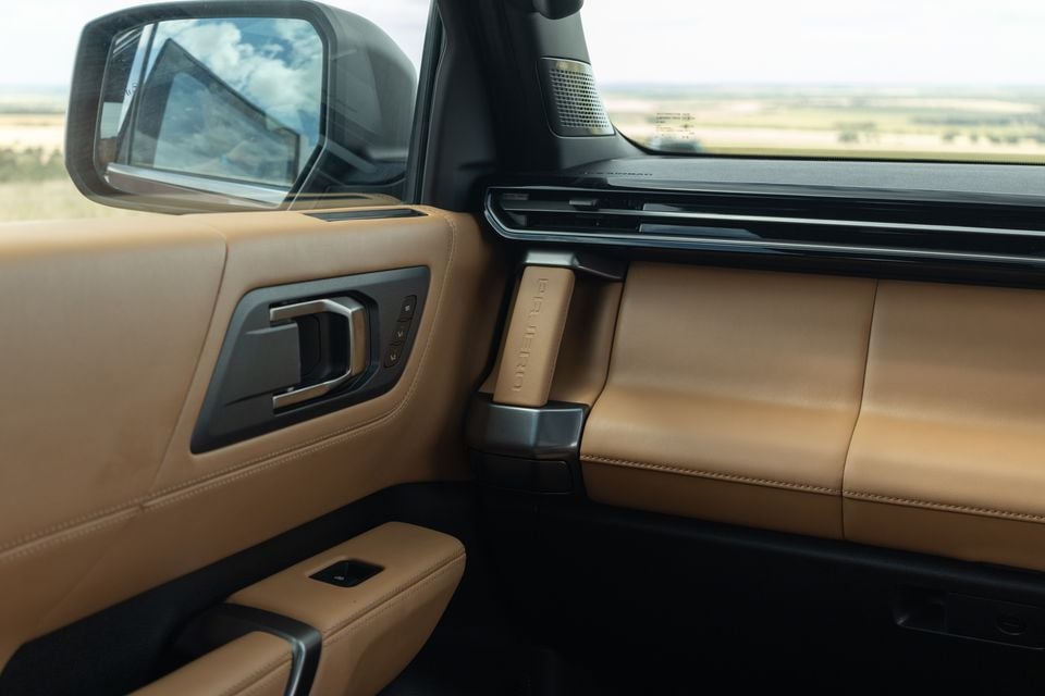 Tan leather front passenger door trim and dashboard of the 2027 Mitsubishi Pajero, with a Pajero-embossed grab handle and side mirror visible