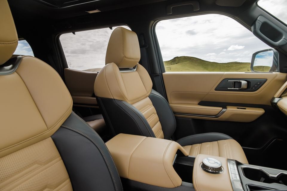 Tan and black leather front seats, centre armrest and console of the 2027 Mitsubishi Pajero, with green hills visible through the windows