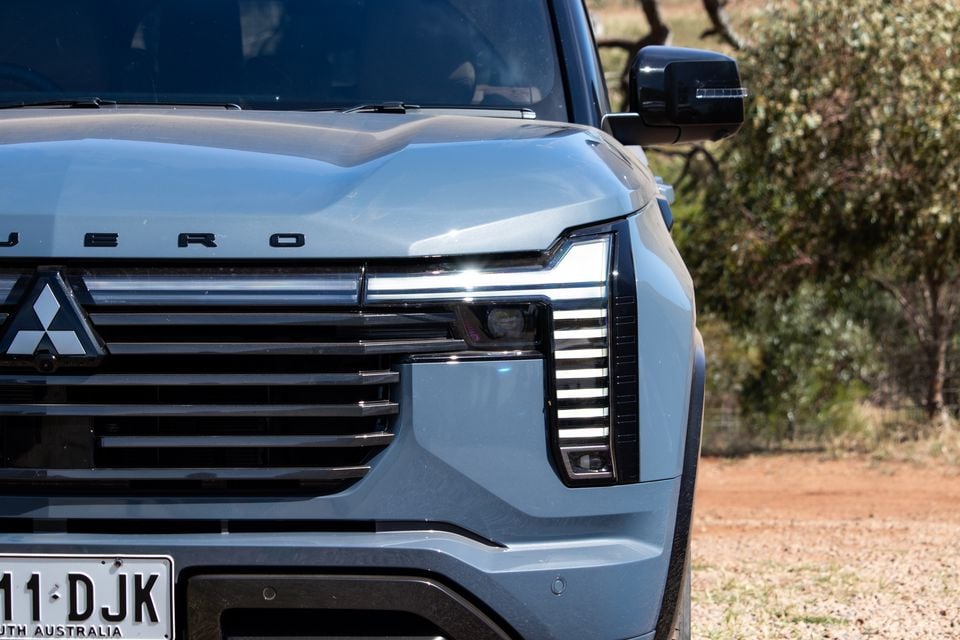 Close-up of the front of a light blue 2027 Mitsubishi Pajero, showing its LED headlight, grille and Mitsubishi badge