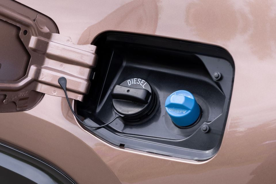 Close-up of an open fuel filler flap on a bronze-coloured vehicle, showing a black diesel fuel cap and a blue AdBlue cap side by side