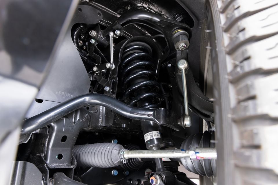 Close-up of a vehicle's front suspension assembly, showing a coil spring, shock absorber, anti-roll bar link, and steering rack components inside the wheel arch