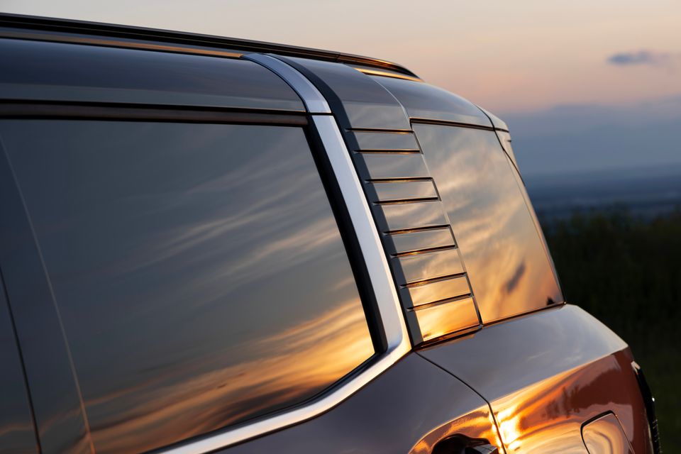 Close-up of the rear quarter window and louvred C-pillar detail on a 2027 Mitsubishi Pajero, reflecting a golden sunset sky