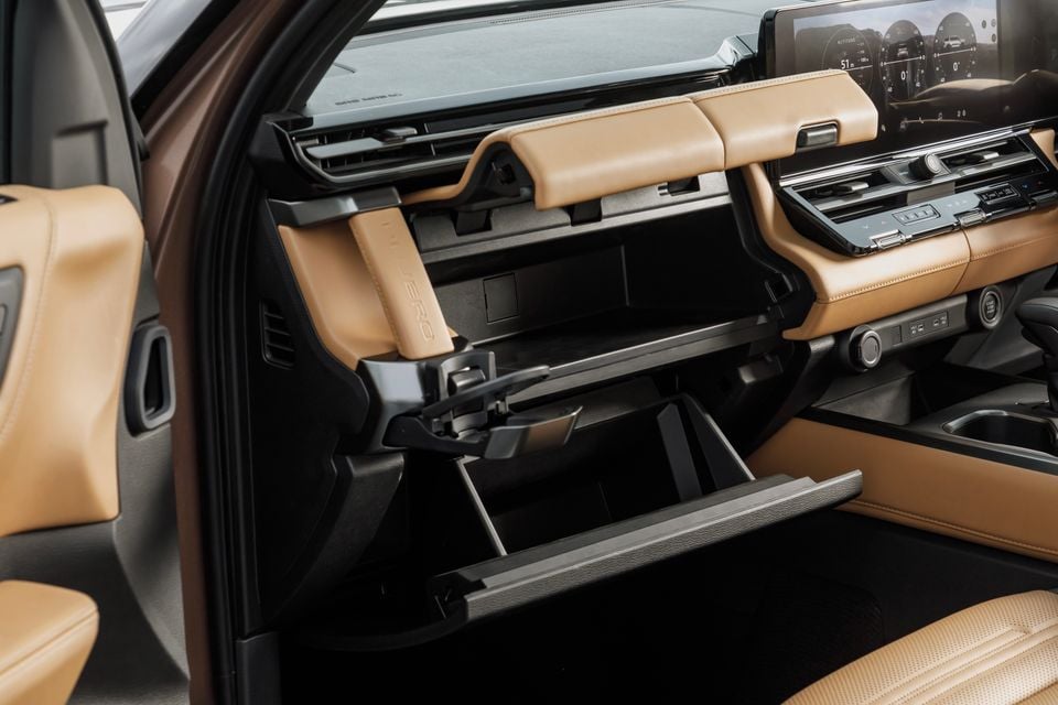 Interior view of the 2027 Mitsubishi Pajero showing the open glove box compartment, tan leather dashboard trim, and centre console with infotainment screen in the background.