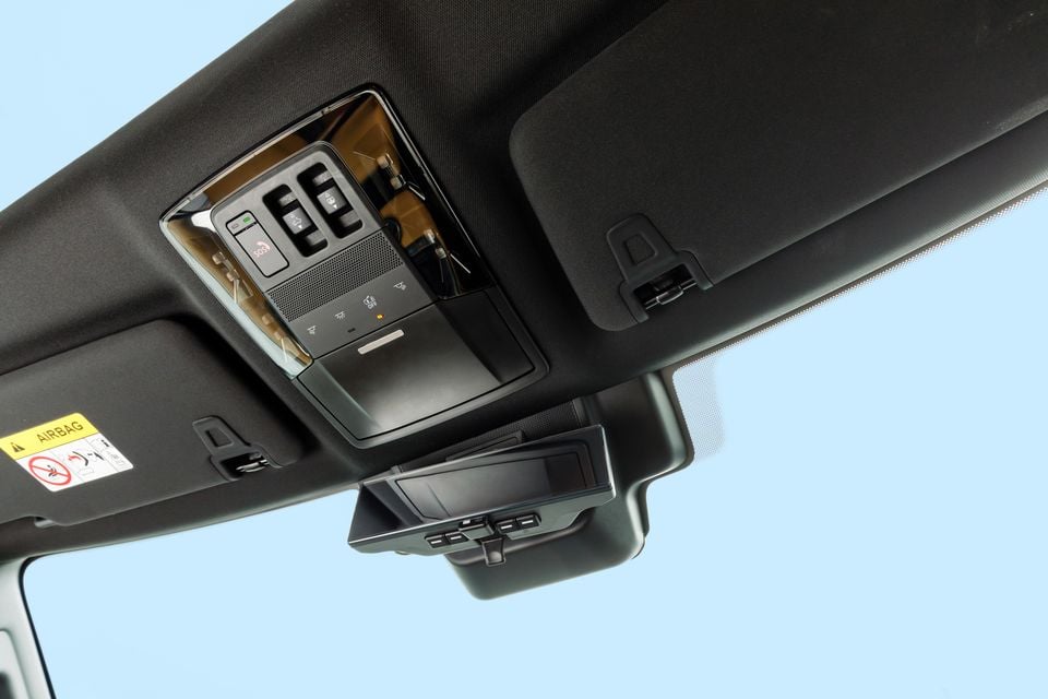 Interior roof lining of a Mitsubishi Pajero showing an overhead console with controls and buttons, sun visors, and a rear-view mirror camera unit.