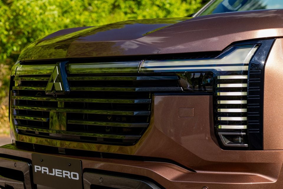 Close-up of the front grille and headlight of a brown Mitsubishi Pajero SUV, showing the Mitsubishi logo and Pajero badging on the bumper