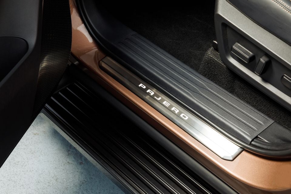 Door sill plate of a Mitsubishi Pajero with the 'Pajero' name embossed, showing the entry area and part of the interior cabin