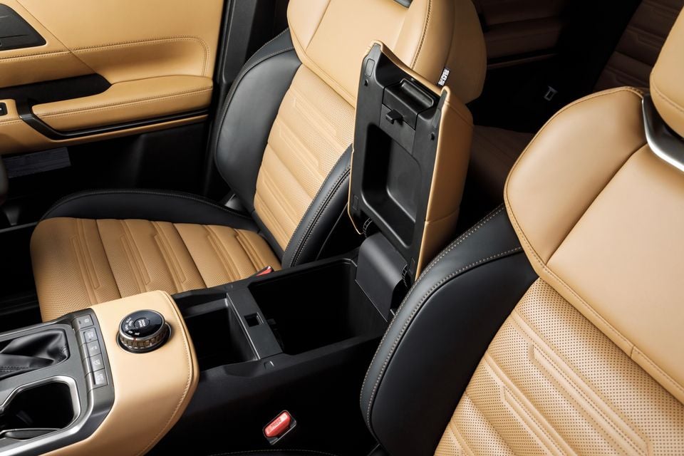 Interior of the 2027 Mitsubishi Pajero showing the centre console storage compartment open, with tan and black leather seats and drivetrain selector controls visible