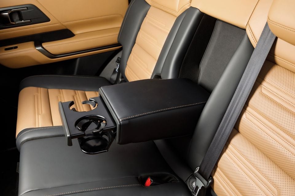 Rear passenger cabin of the 2027 Mitsubishi Pajero showing a black centre armrest with fold-out cup holders and tan leather seats with seatbelts