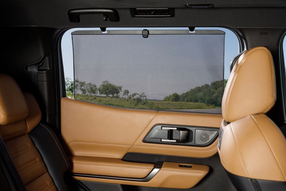 Interior view of a car's rear passenger area showing tan leather seats and door panel with a retractable window sunshade deployed