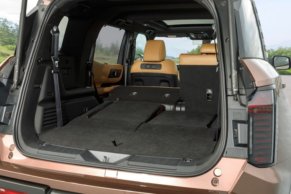 Boot of a 2027 Mitsubishi Pajero SUV with the third-row seats folded flat to reveal a large, carpeted cargo area, viewed from the rear with tan leather second-row seats visible