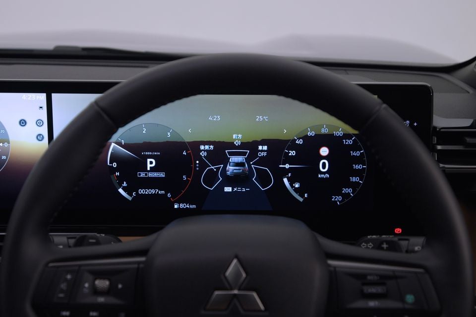 Mitsubishi Pajero digital instrument cluster and steering wheel, showing speedometer, tachometer and a surround-view camera display on the driver's screen