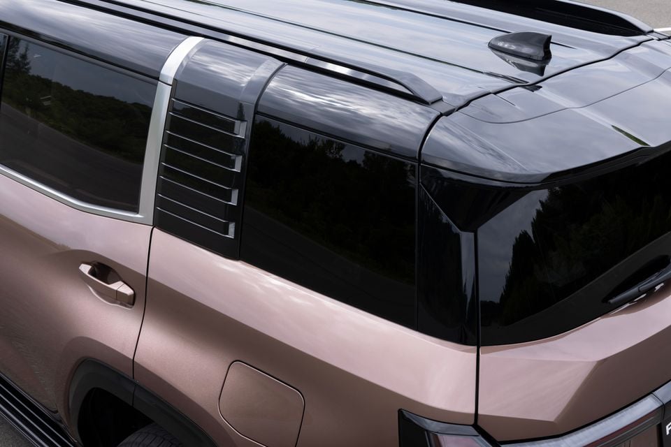 Close-up of the upper body and roofline of a bronze-coloured 2027 Mitsubishi Pajero SUV, showing louvred rear quarter window, black roof panel, shark fin antenna, and door handle detail