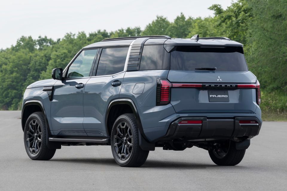 A grey 2027 Mitsubishi Pajero SUV seen from the rear three-quarter angle, parked on a road with trees in the background.