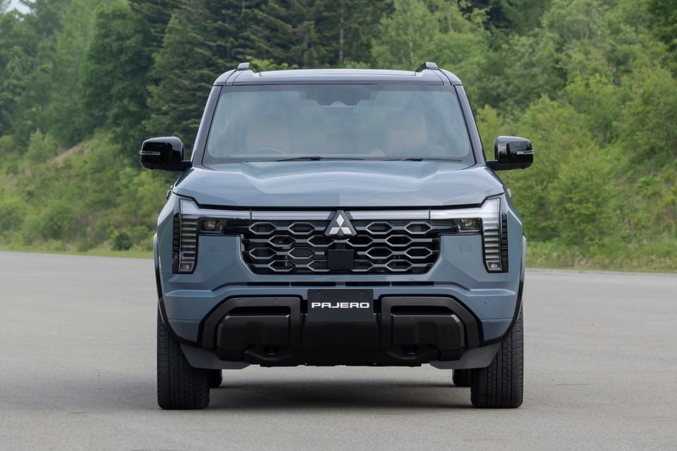 A Mitsubishi Pajero SUV seen from the front, finished in dark blue-grey, parked on a road surrounded by trees.