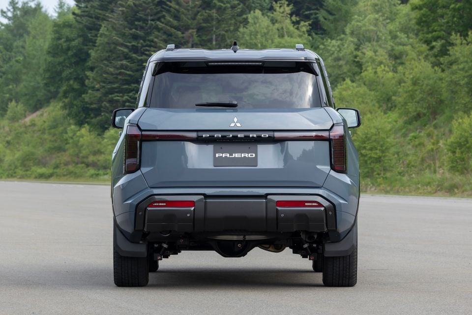 Rear view of a grey 2027 Mitsubishi Pajero SUV parked on a road surrounded by trees