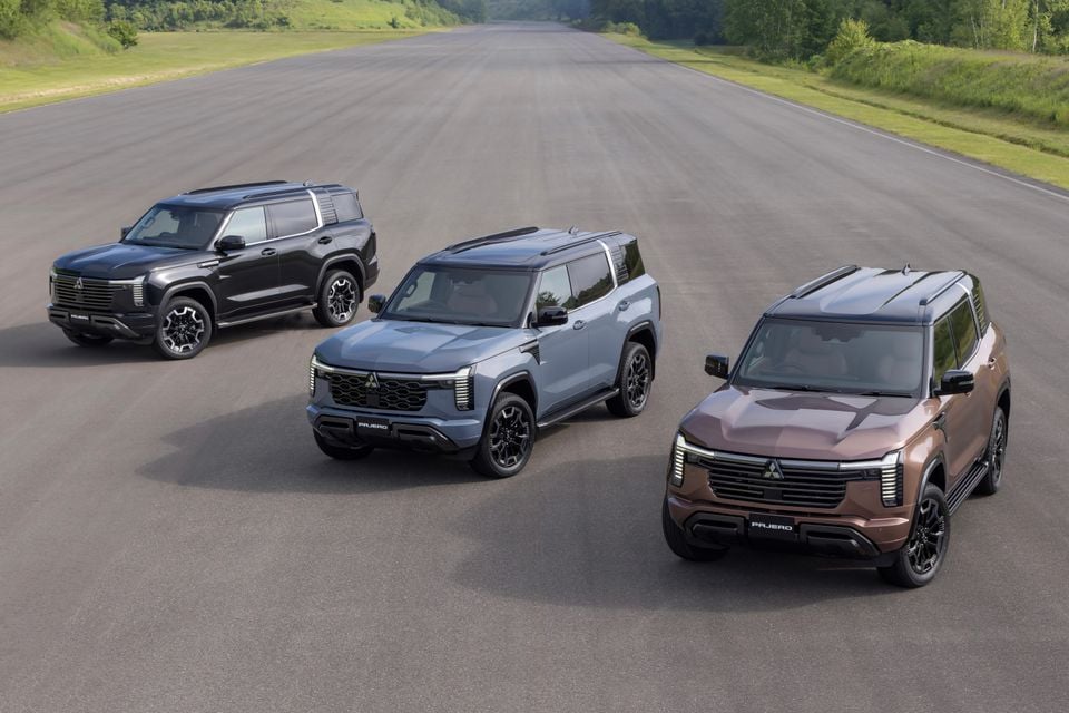 Three Mitsubishi Pajero SUVs in black, grey-blue, and brown displayed on an open tarmac, showing front and front-side angles