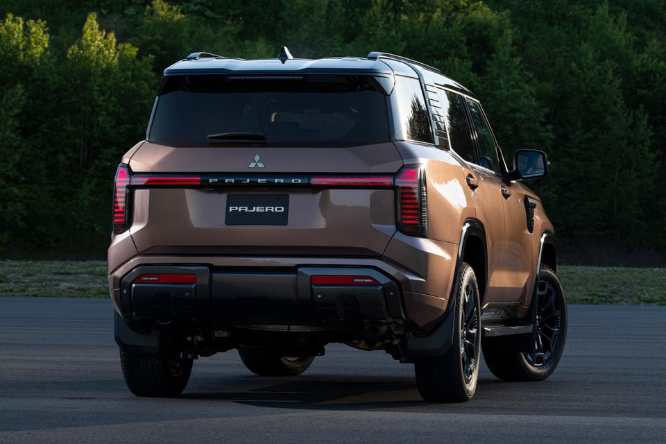 Rear view of a bronze 2027 Mitsubishi Pajero SUV parked on a paved surface with trees in the background