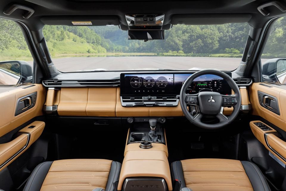 Interior of the Mitsubishi Pajero showing tan leather seats, a wide dual-screen infotainment and instrument display, and centre console with rotary drive mode selector