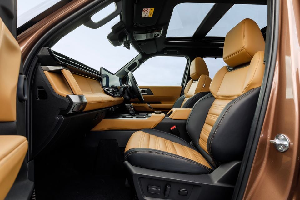 The front interior cabin of the 2027 Mitsubishi Pajero, showing two-tone tan and black leather front seats, centre console, touchscreen infotainment display, and panoramic sunroof overhead.