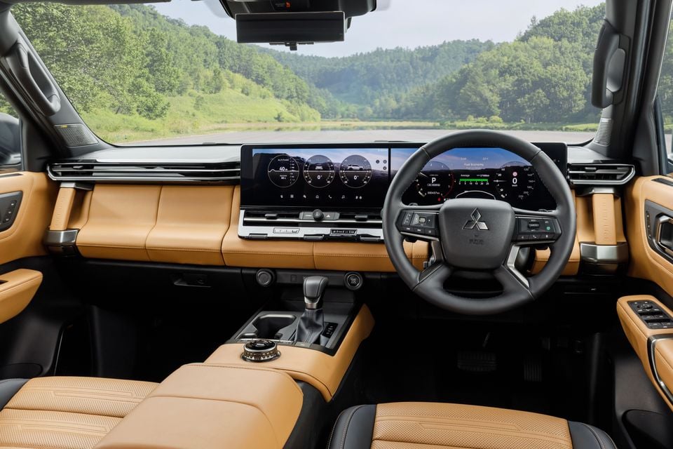 Interior of the 2027 Mitsubishi Pajero showing tan leather seats, a wide dual digital display screen, Mitsubishi steering wheel, and centre console with gear shifter