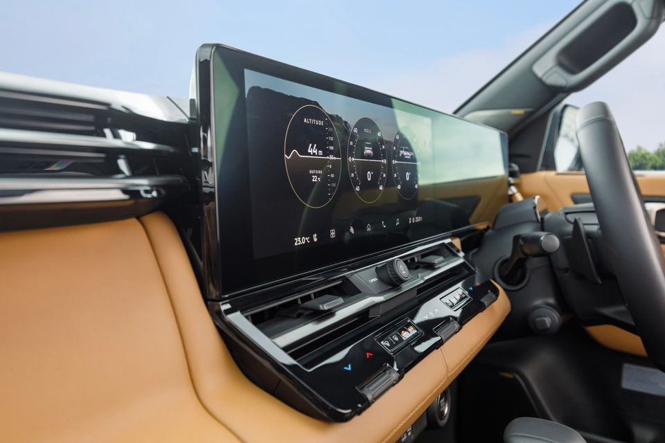 The wide touchscreen infotainment display inside the 2027 Mitsubishi Pajero, showing altitude, roll, and pitch gauges alongside climate controls and tan leather interior trim.