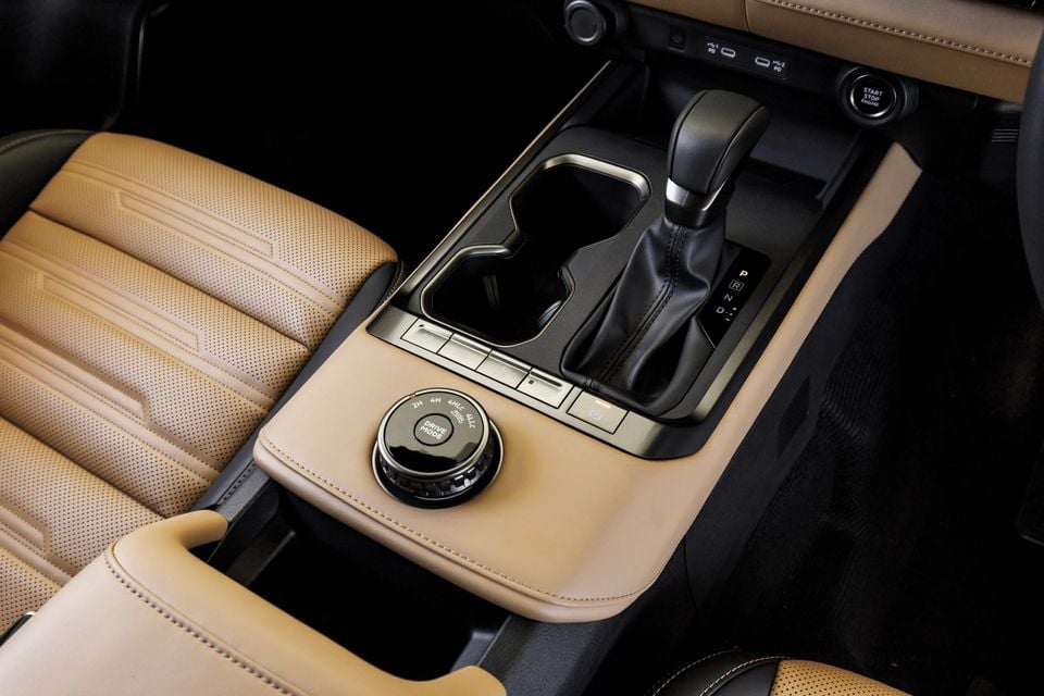 Interior centre console of the 2027 Mitsubishi Pajero showing the gear shifter, drive mode selector dial with 2H, 4H, 4HLC and 4LLC settings, and tan leather trim