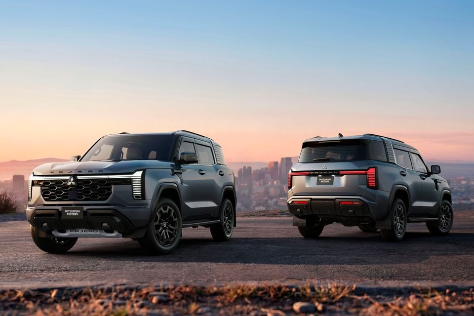 Two Mitsubishi Pajero SUVs shown from the front and rear against a city skyline at sunset