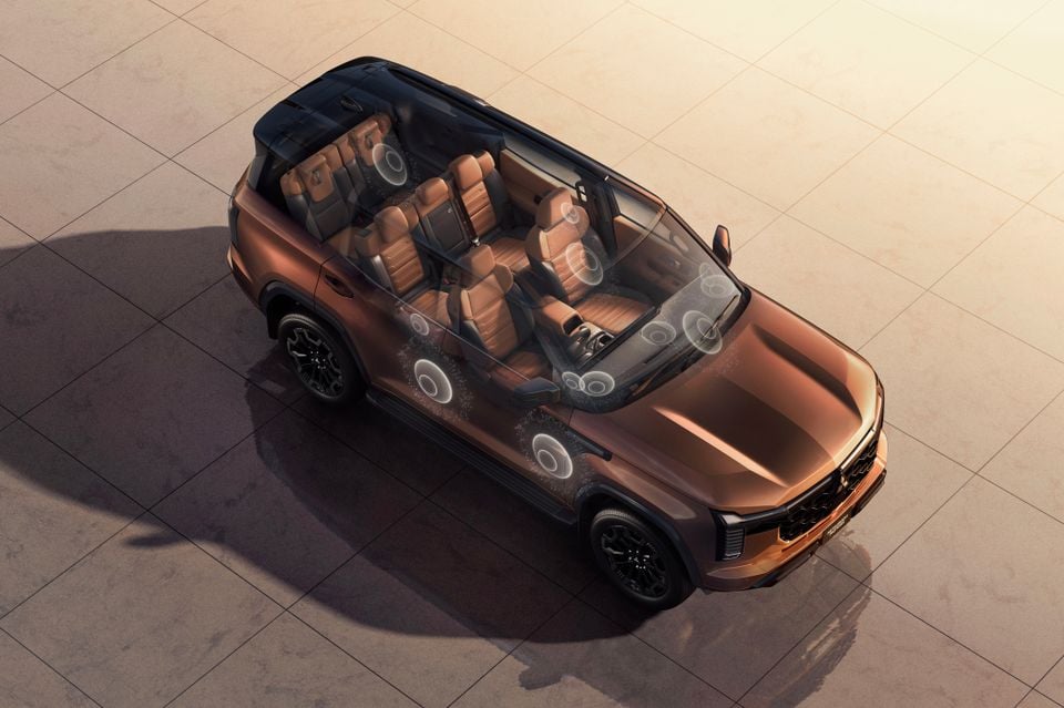 Overhead view of a bronze Mitsubishi Pajero SUV with a transparent roof graphic revealing the multi-row interior and speaker placement throughout the cabin