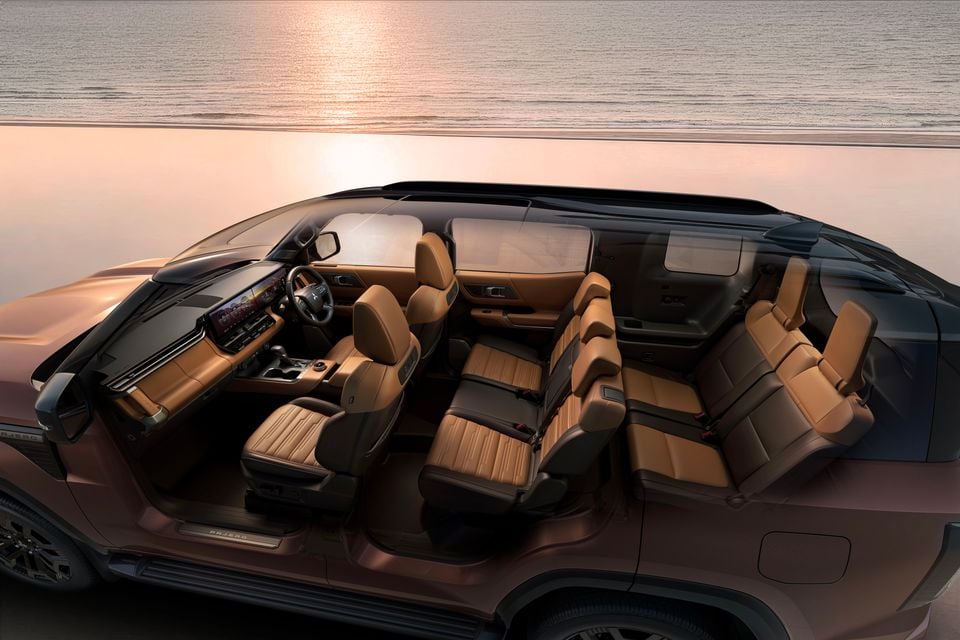 A cutaway-style render of the 2027 Mitsubishi Pajero SUV showing the tan and dark brown leather three-row interior cabin, dashboard, and large infotainment screen, seen from the side against a sunset backdrop.