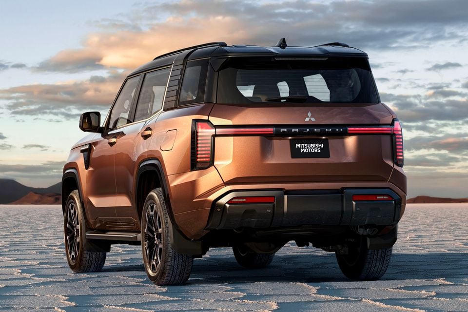 A bronze 2027 Mitsubishi Pajero SUV seen from the rear three-quarter angle on a salt flat at sunset.