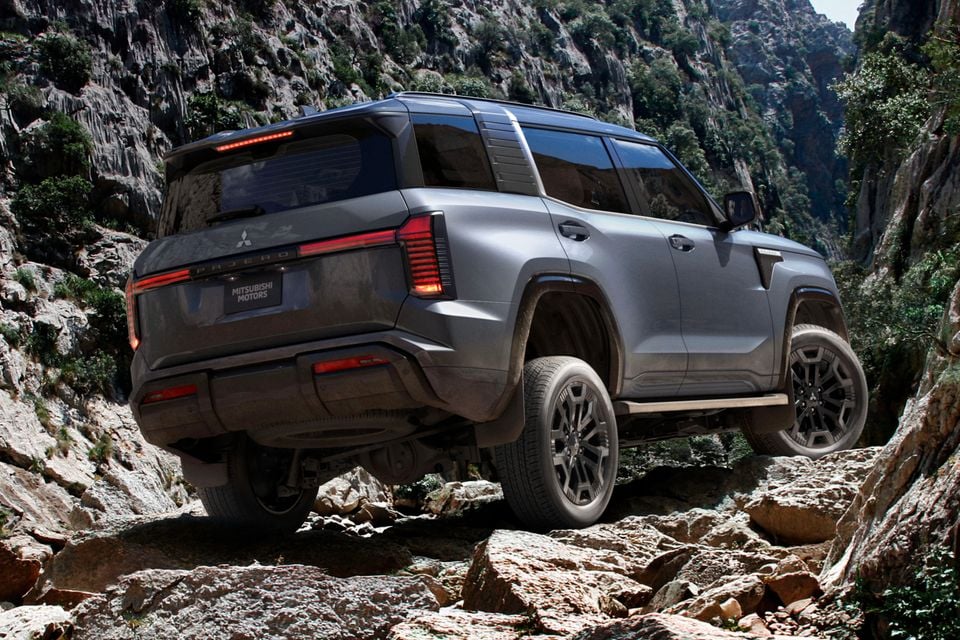 A grey Mitsubishi Pajero SUV navigating rocky terrain in a canyon, seen from the rear three-quarter angle