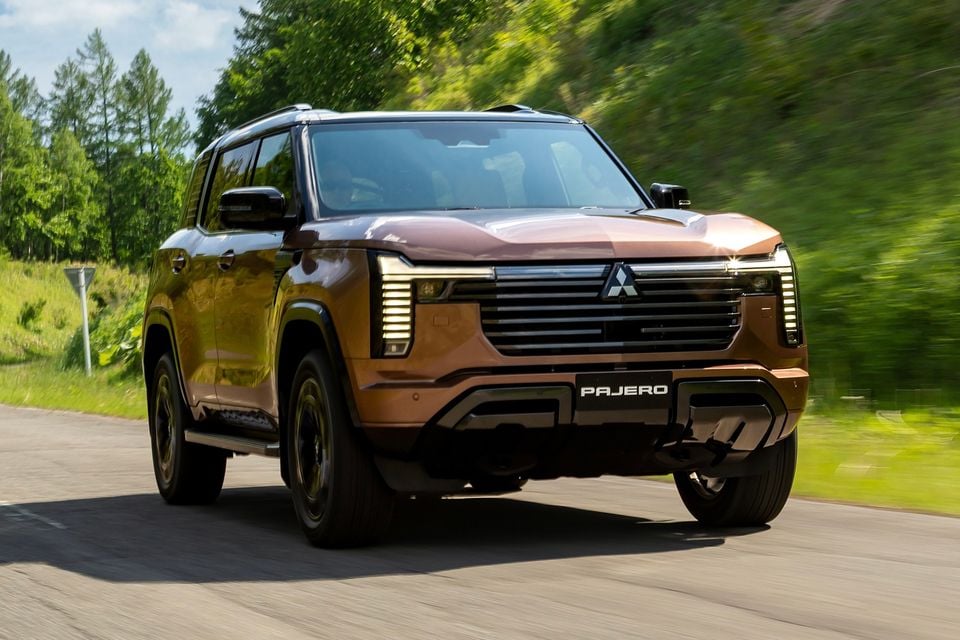 A bronze Mitsubishi Pajero SUV driving along a road, seen from the front at a slight angle