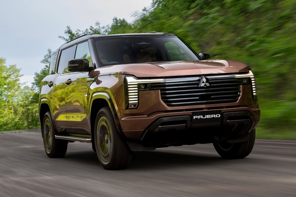 A bronze Mitsubishi Pajero SUV driving along a road, seen from the front three-quarter angle