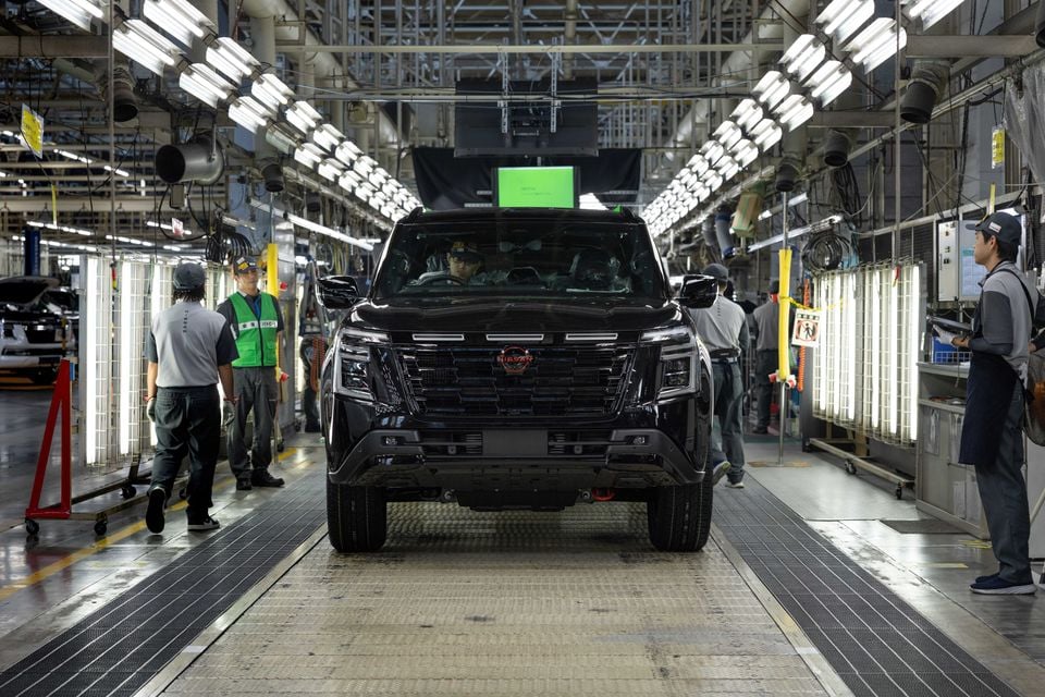 A black 2027 Nissan Patrol SUV seen from the front on a factory production line, with workers standing alongside