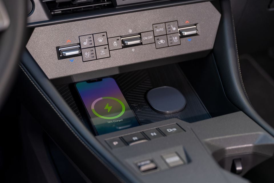 A smartphone wirelessly charging at 76% in the centre console of a 2027 Nissan Rogue Hybrid, with climate and seat controls visible above