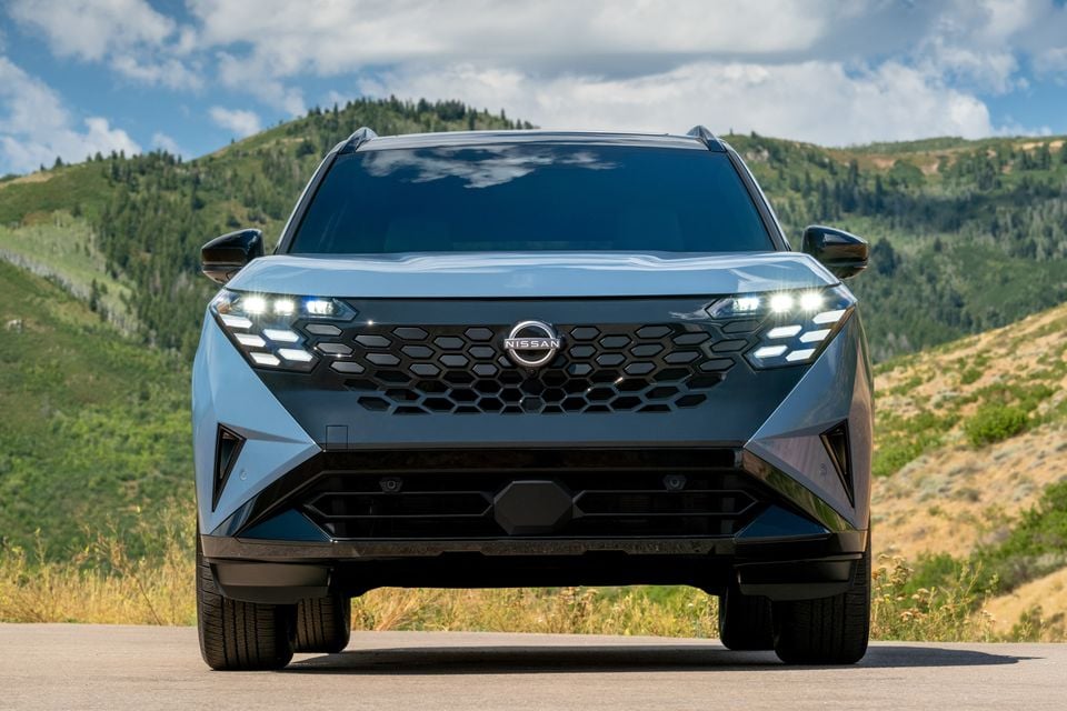 Front view of a 2027 Nissan Rogue Hybrid SUV on a road with green hills in the background