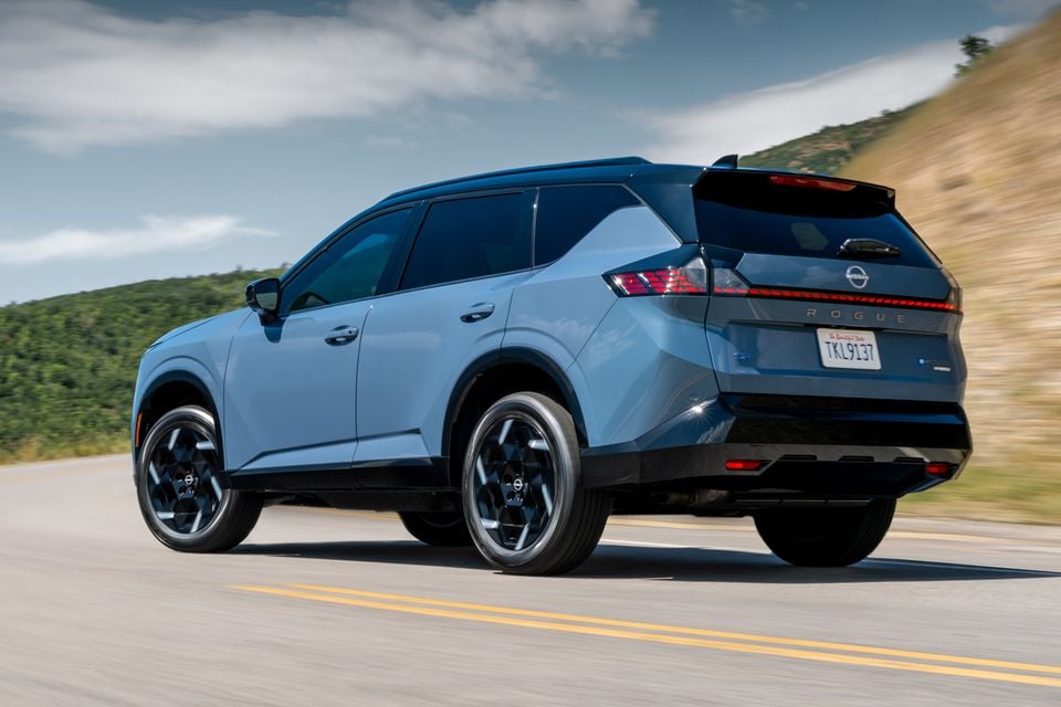 A blue 2027 Nissan Rogue Hybrid SUV seen from the rear three-quarter angle while driving on a road