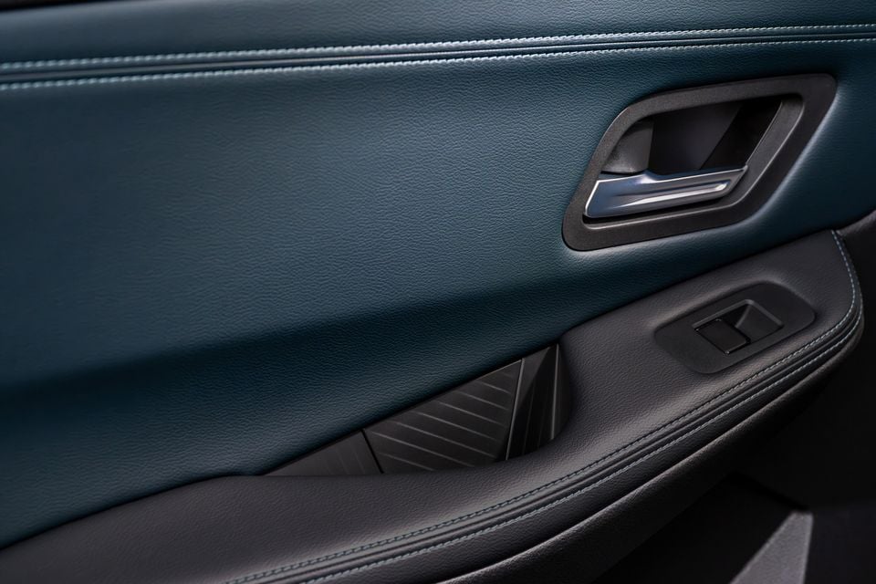 Close-up of a car door panel interior showing teal leather upholstery with contrasting stitching, an interior door handle with chrome trim, and window control switches