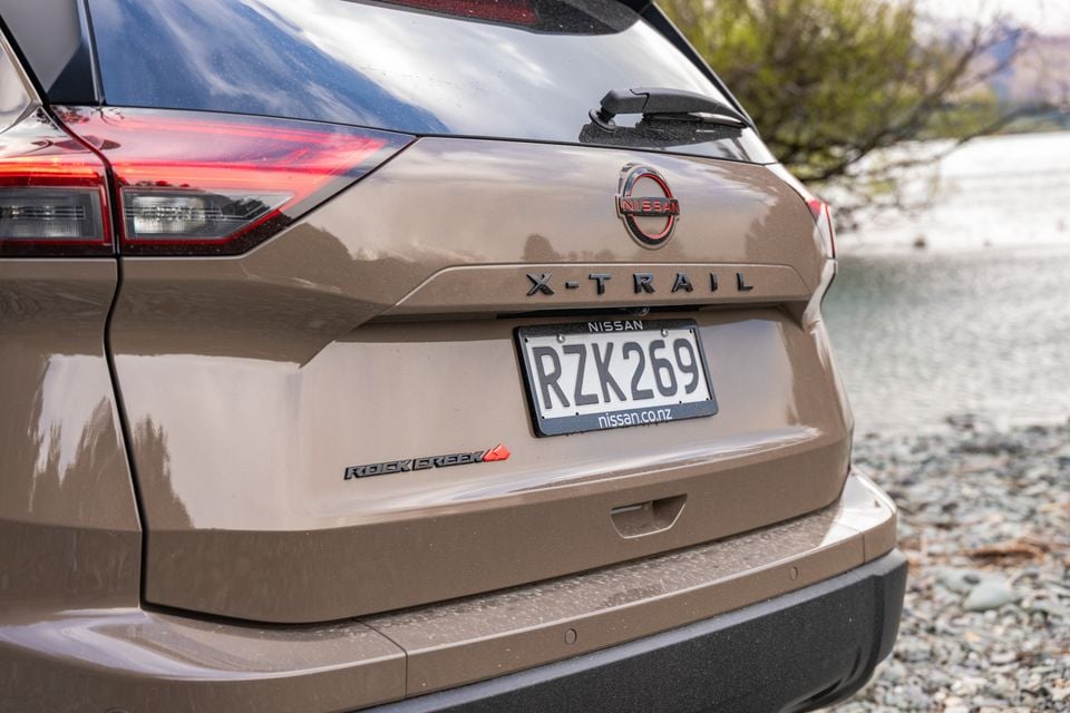 Close-up of the rear badge and tailgate of a bronze Nissan X-Trail Rock Creek, showing the Nissan logo, X-Trail lettering and number plate