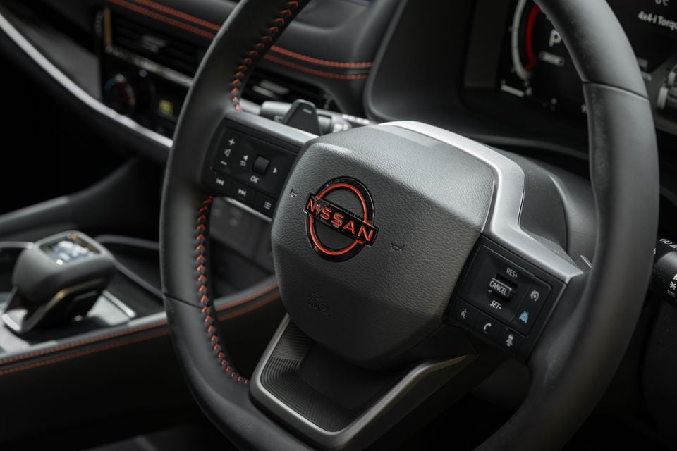 Close-up of the steering wheel and Nissan badge inside a 2027 Nissan X-Trail, showing control buttons and part of the instrument cluster.