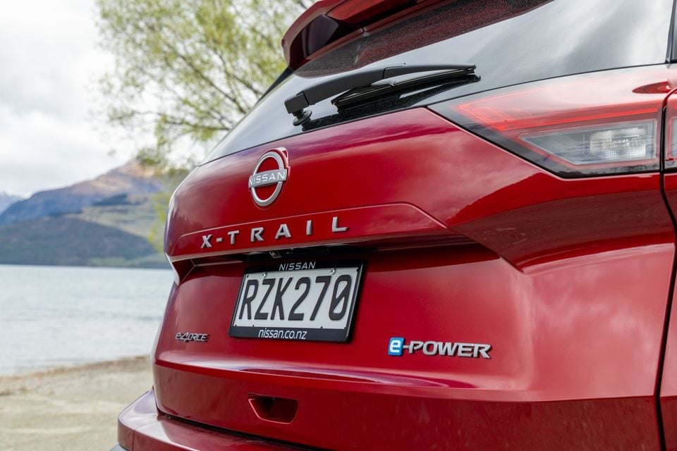 Close-up of the rear badge and taillight on a red Nissan X-Trail e-Power, parked near a lake