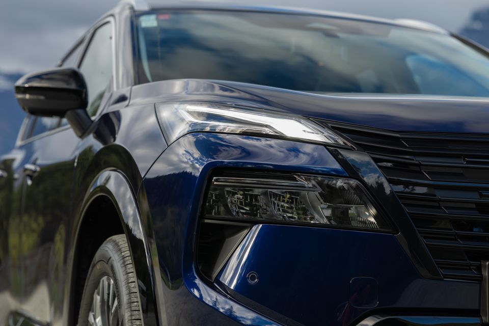 Close-up of the headlight and front grille on a dark blue 2027 Nissan X-Trail Ti-L e-Power SUV
