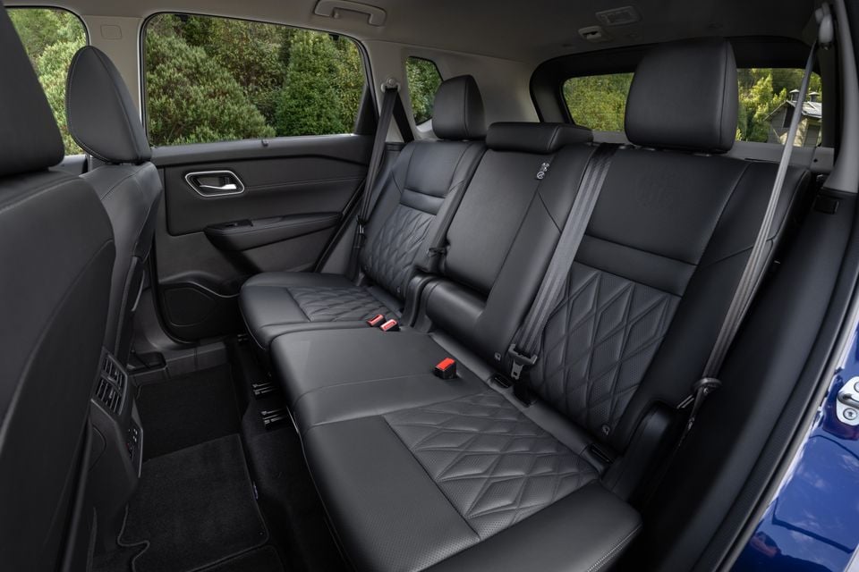 The black leather rear seats of a 2027 Nissan X-Trail Ti-L, seen through the open door with seatbelts and a parcel shelf visible.
