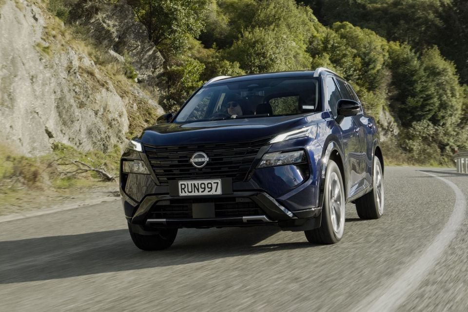 A dark blue Nissan X-Trail SUV driving on a winding mountain road, seen from the front quarter